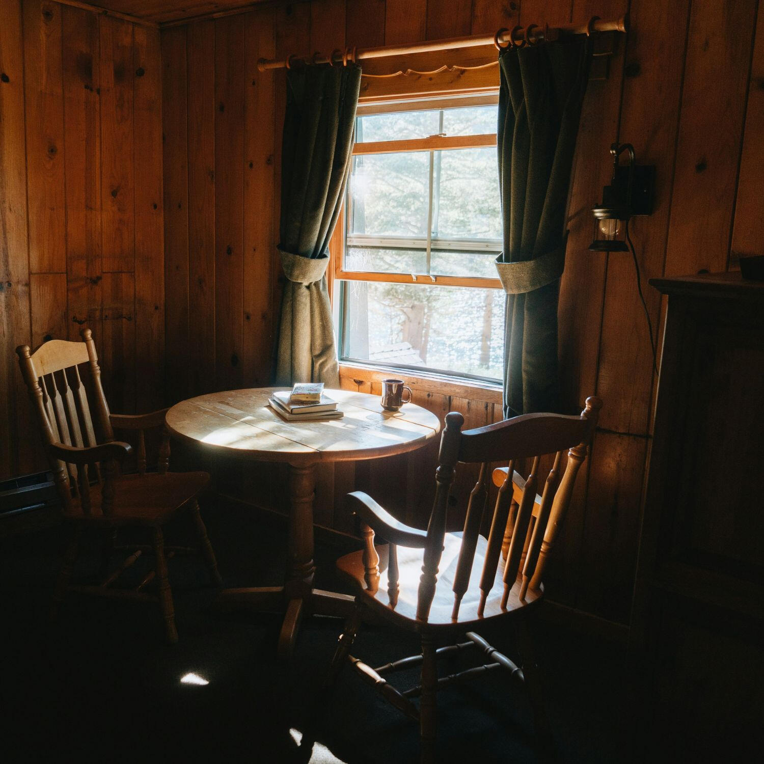 rustic-cabin-quiet-reflection-table-books Rustic wooden table and chairs in a cozy cabin corner with natural light, books, and a warm, peaceful atmosphere for quiet reflection